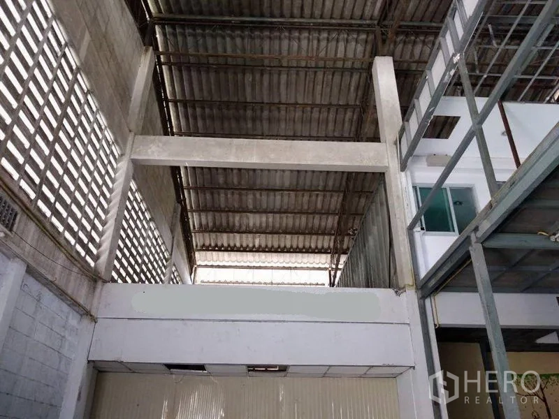 Warehouse for rent in Mueang Nonthaburi, Nonthaburi - High-ceiling warehouse with ventilated block walls, corrugated metal roof and mezzanine walkway beside a windowed office.