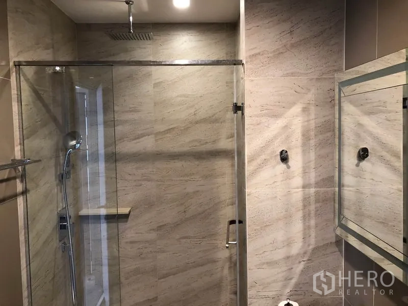 Condominium for rent in Watthana, Bangkok - Glass‑enclosed rainfall shower with stone‑texture tiles and chrome fixtures.