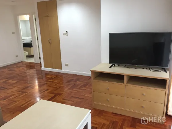 公寓 出租在Watthana, Bangkok - 起居区配电视与木质抽屉柜，内置储物柜，通往卫浴的门与光亮木地板。