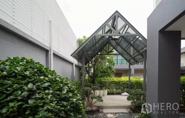 Detached House for rent or sale in Saphan Sung, Bangkok - Shaded garden pavilion with a glass roof beside lush hedges.