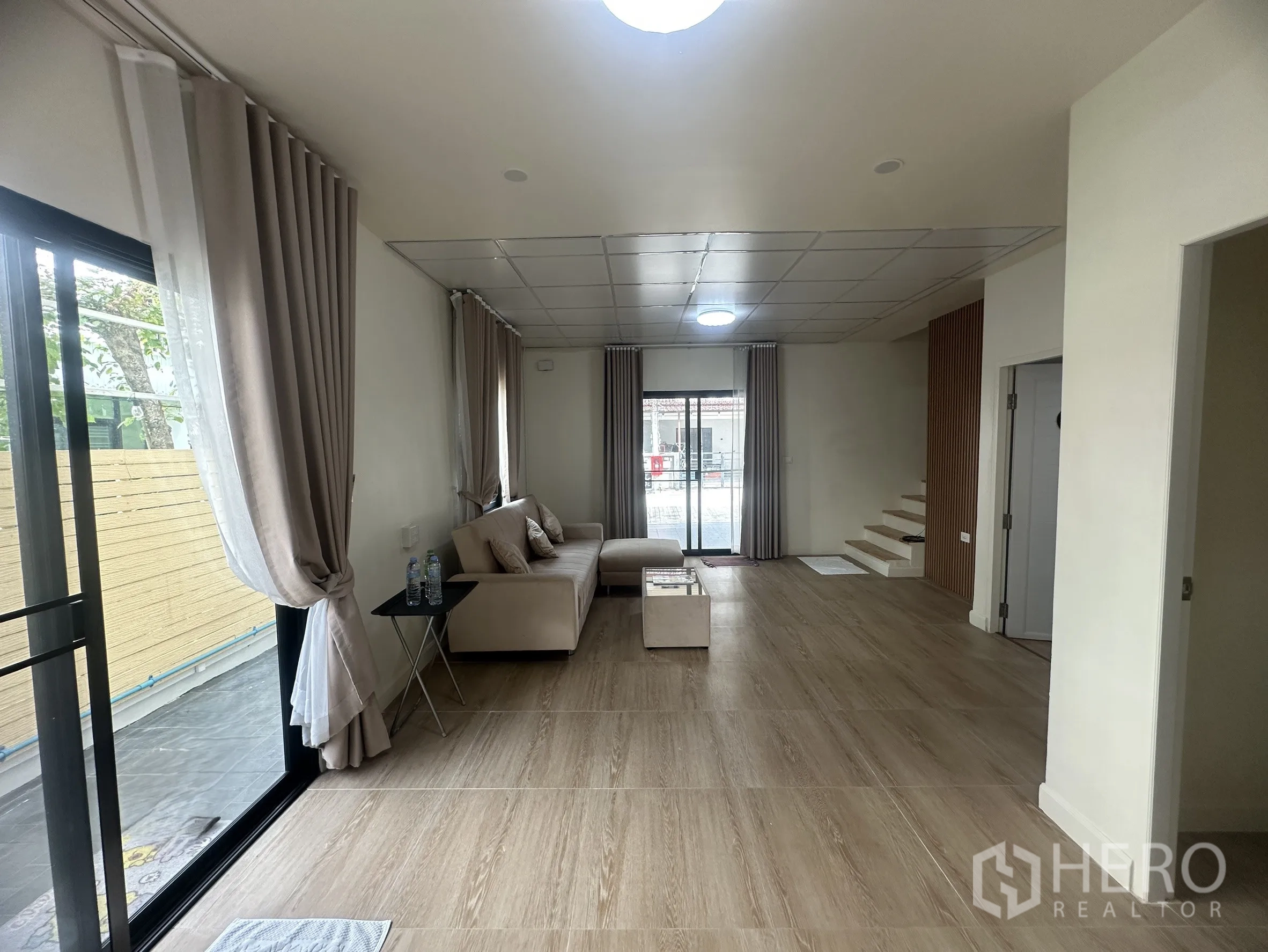 Townhouse for sale in Lam Luk Ka, Pathum Thani - Open-plan living room facing large sliding glass doors and side windows.