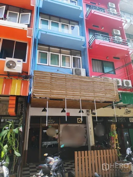 联排别墅 出租在Sathon, Bangkok - 多彩商住楼立面中的蓝色联排别墅，带阳台与雨棚，街景热闹。
