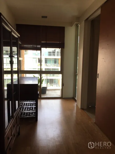 Condominium for rent in Khlong Toei, Bangkok - Bright room with wooden floor and floor-to-ceiling windows opening to a balcony.