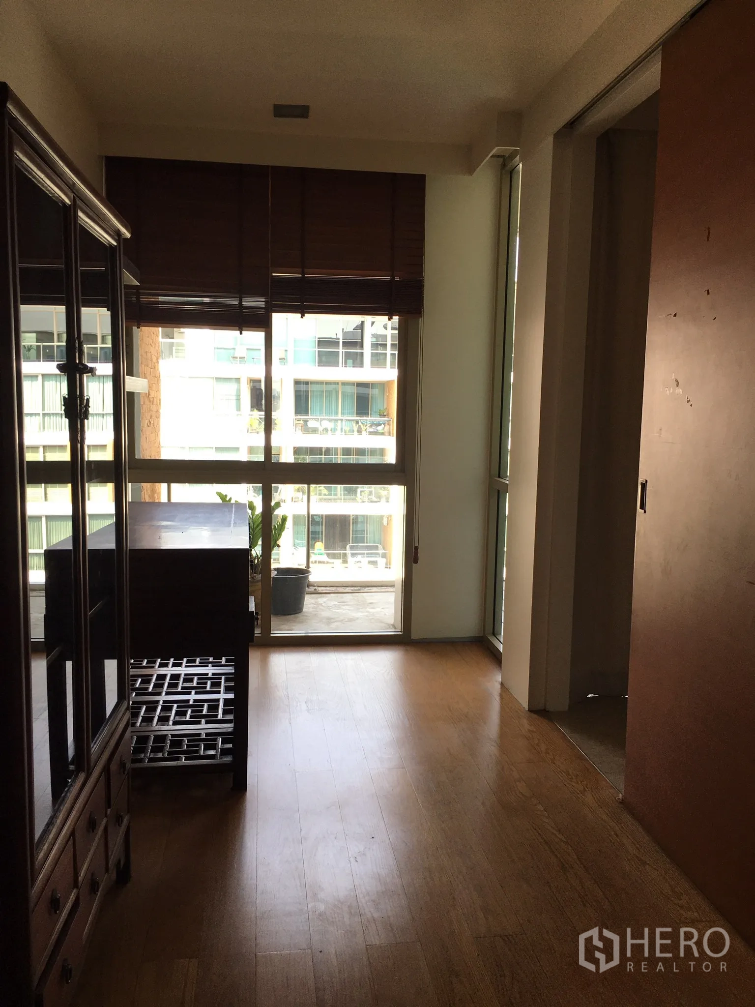 Condominium for rent in Khlong Toei, Bangkok - Bright room with wooden floor and floor-to-ceiling windows opening to a balcony.