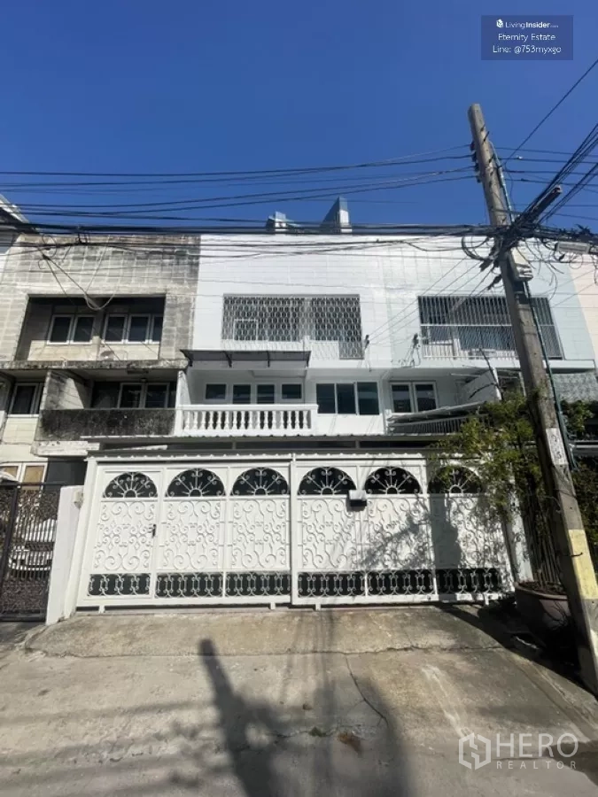 带办公室的家 出租在Khlong Toei, Bangkok - 三层联排外立面，装饰性铁艺大门与阳台，蓝天映衬。