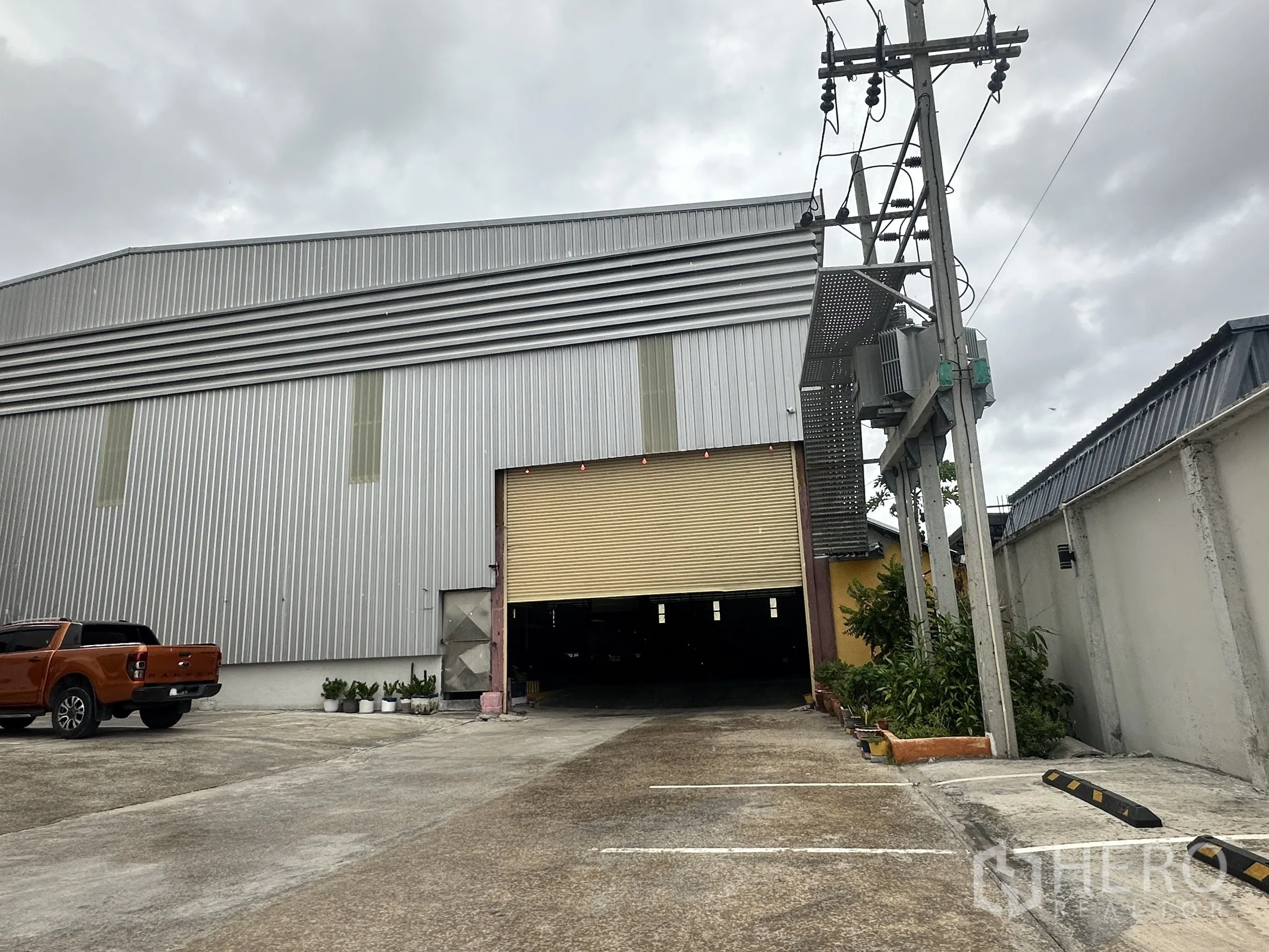 仓库 for rent in Mueang Samut Prakan, Samut Prakan - 入口区带卷闸门，划线停车位与围墙环绕场地。
