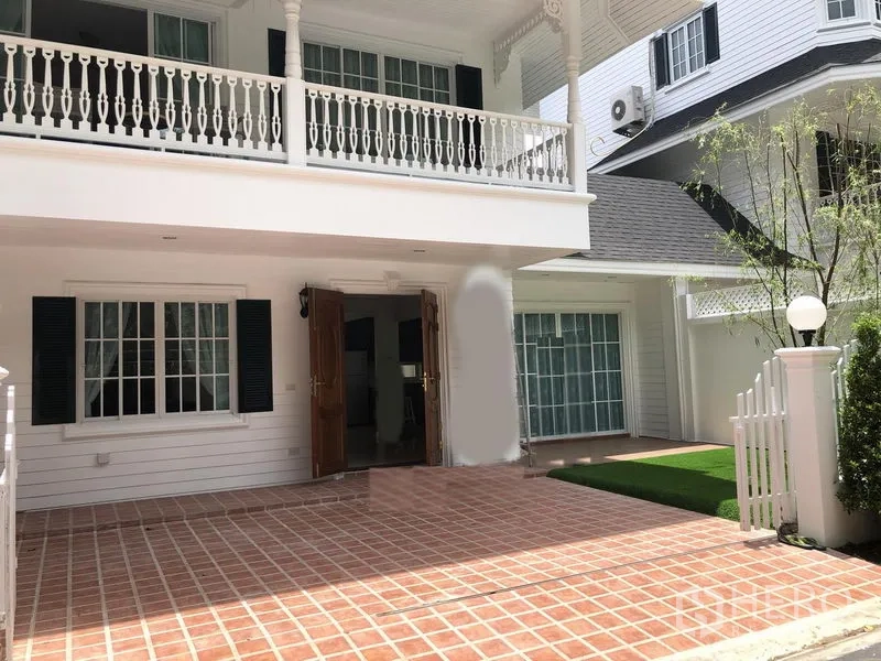 Detached House for rent in Mueang Samut Prakan, Samut Prakan - Two-storey white detached house with balcony, tiled carport and small lawn behind a white picket fence.