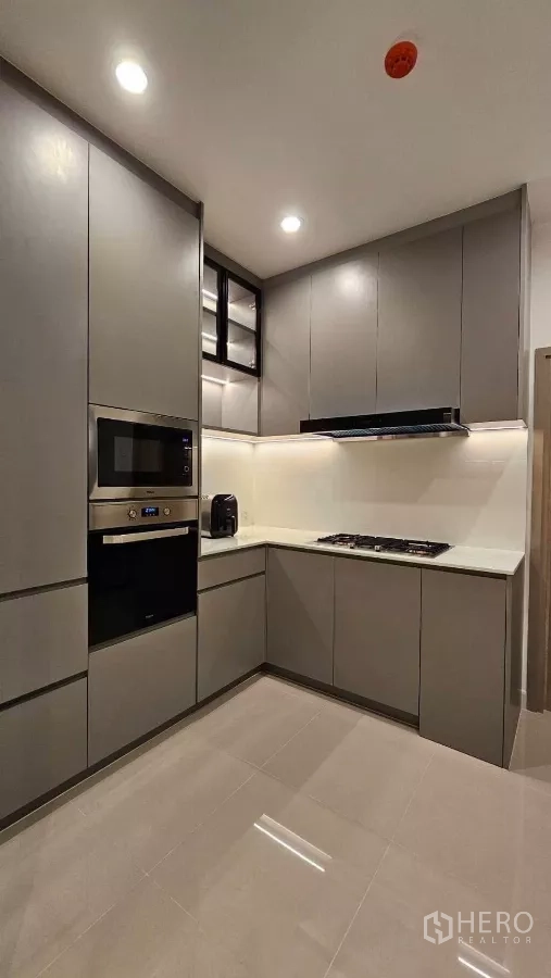 Detached House for rent or sale in Prawet, Bangkok - Separate Thai kitchen with L-shaped counters, gas hob, built-in oven and dark cabinetry.