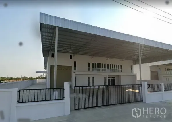 工厂 出租或出售在Bang Bo, Samut Prakan - 工厂外立面斜角视图，金属屋顶遮棚、深进深车道与黑色推拉门。