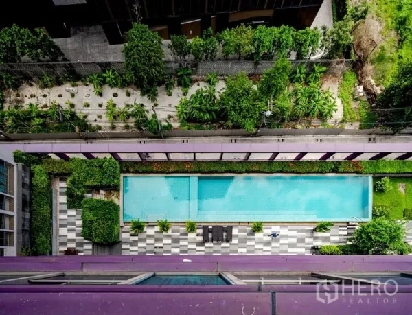 Condominium for sale in Khlong Toei, Bangkok - Aerial view of a long outdoor swimming pool with sun deck surrounded by landscaped greenery.