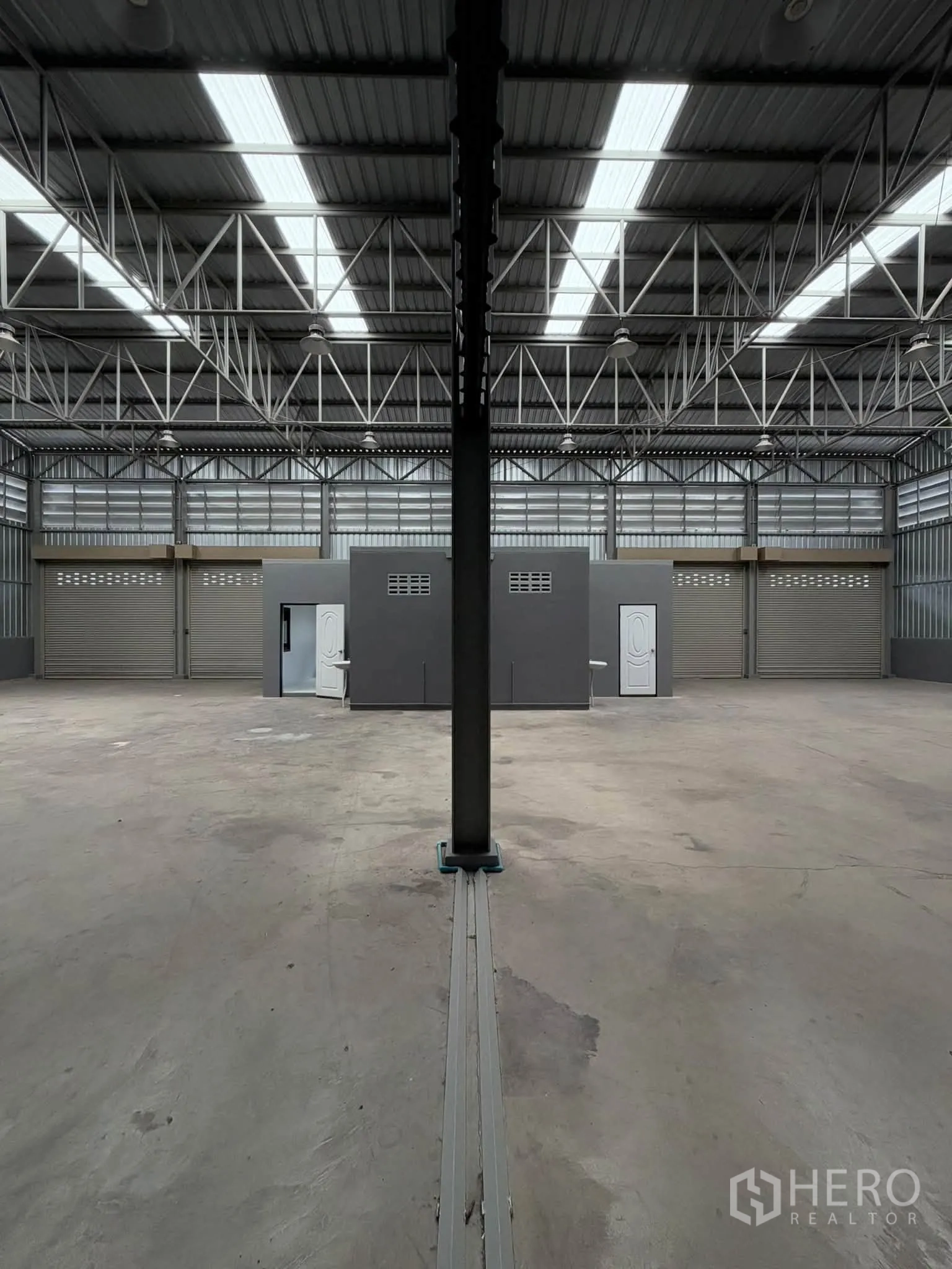Warehouse for rent in Phra Pradaeng, Samut Prakan - Wide warehouse bay with central support column, skylights, and office blocks facing multiple shutter doors.