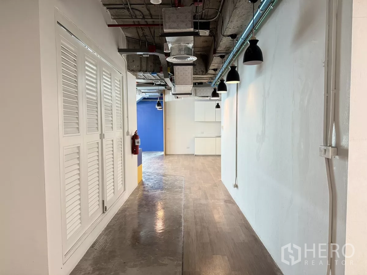 Office Space for rent in Din Daeng, Bangkok - Corridor with industrial ceiling, wall sconces, storage cabinets, and mixed concrete and wood flooring.