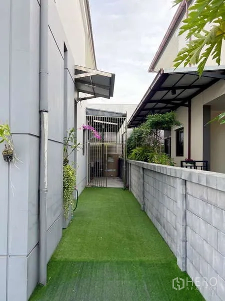 独立式住宅 出售在Prawet, Bangkok - 狭长侧院步道，人工草坪与隐私围墙，后方为遮雨服务区。