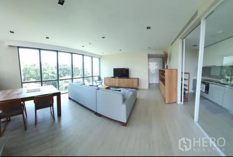 公寓 出租或出售在Watthana, Bangkok - 开放式客餐厅，落地窗、L形沙发与电视柜，旁连玻璃隔断厨房，位于瓦塔那公寓