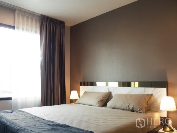คอนโด ให้เช่าในHuai Khwang, Bangkok - ห้องนอนสว่าง เตียงคู่ โคมไฟข้างเตียง และหน้าต่างบานใหญ่พร้อมผ้าม่านในคอนโดห้วยขวาง