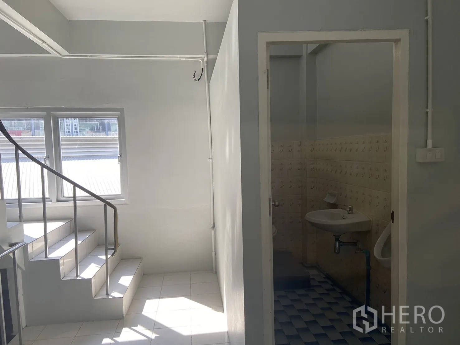 Shophouse for rent in Bang Na, Bangkok - Bright stairwell with windows beside the entrance to a tiled restroom.