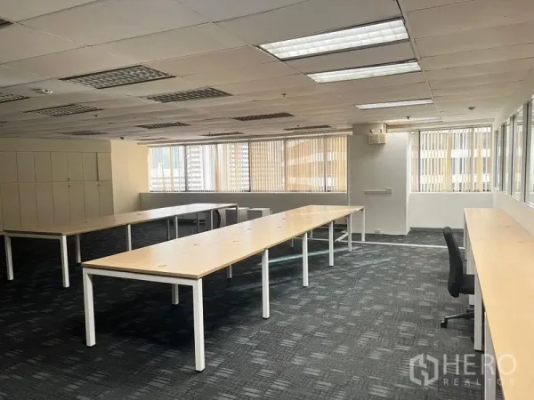 办公空间 出租在Khlong Toei, Bangkok - 开放式办公室，长条工作台、地毯地面、明亮的吊顶灯和带百叶的大窗。