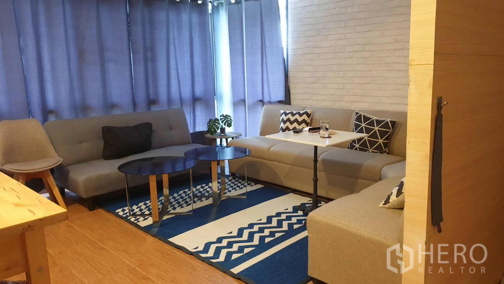 บ้านเดี่ยว for rent in Watthana, Bangkok - ห้องนั่งเล่นอบอุ่นด้วยโซฟาสีเทา โต๊ะกลางทรงกลม พรมลาย และผ้าม่านทึบ.