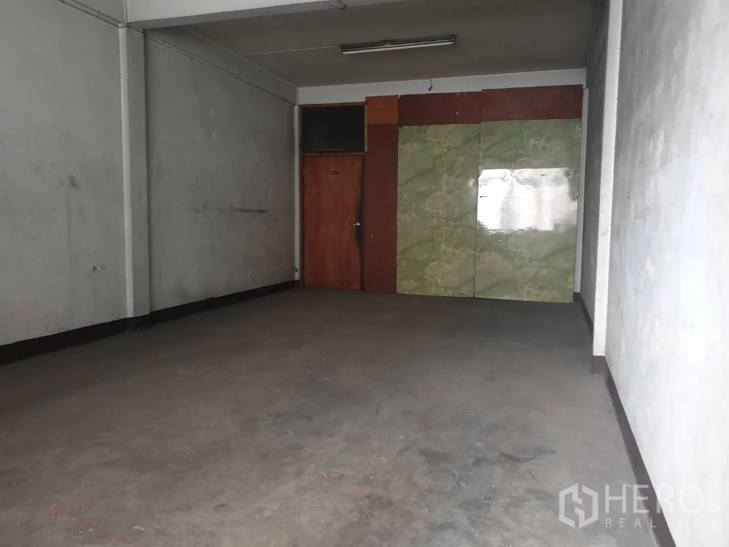 店屋 出租在Phra Khanong, Bangkok - 空置的混凝土房间，灰色墙面与木门，适合作仓储或工作区。
