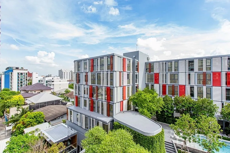 公寓 出租在Watthana, Bangkok - 低层现代公寓外观，红白立面点缀，被绿树和城市景观环绕。
