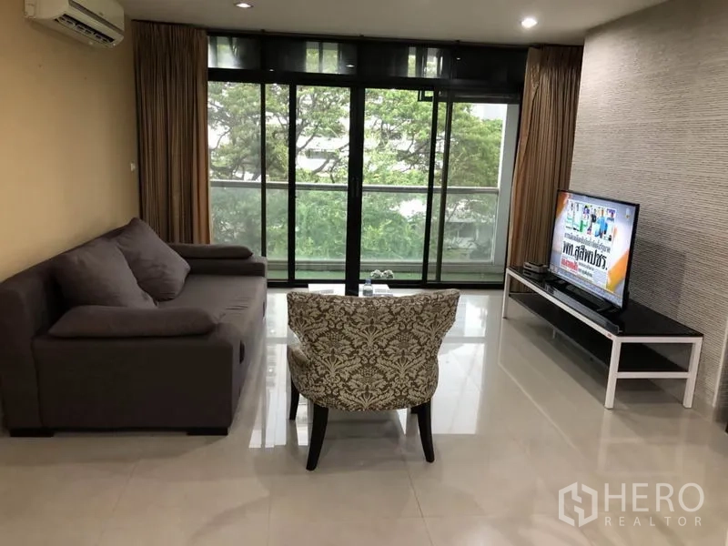 Condominium for rent in Watthana, Bangkok - Spacious Watthana condo living room with sofa, TV and a balcony overlooking greenery.
