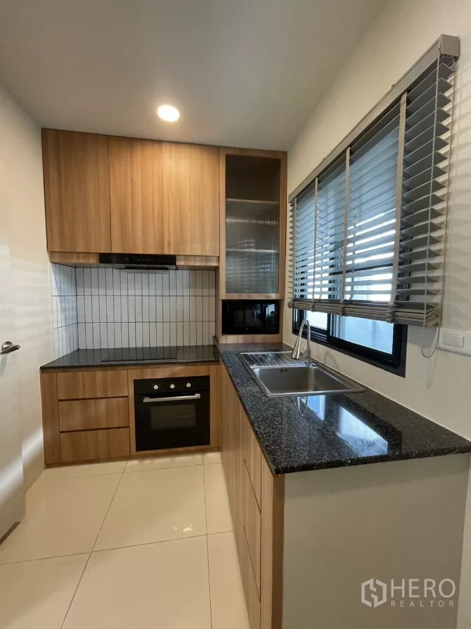 独立式住宅 出租在Bang Phli, Samut Prakan - 一字型木作厨房，黑色花岗岩台面，烤箱与小白砖墙面。