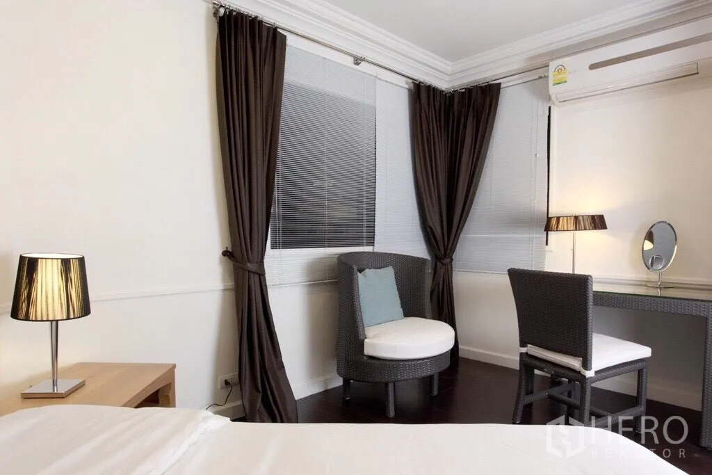 Condominium for rent in Sathon, Bangkok - Bedroom corner with vanity desk, round lounge chair, and floor-to-ceiling curtains.