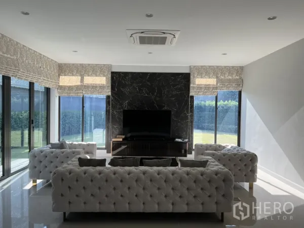 Detached House for rent in Bang Kapi, Bangkok - Bright living room with tufted sofas, a marble TV feature wall, and sliding glass doors.