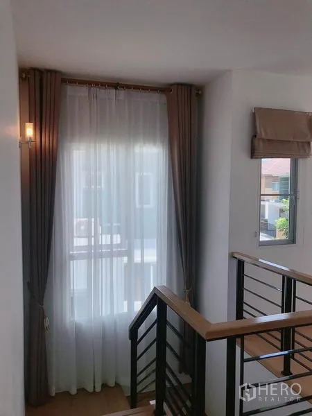 Detached House for sale in Suan Luang, Bangkok - Bright stairwell with windows, wooden handrail and flowing sheer curtains.