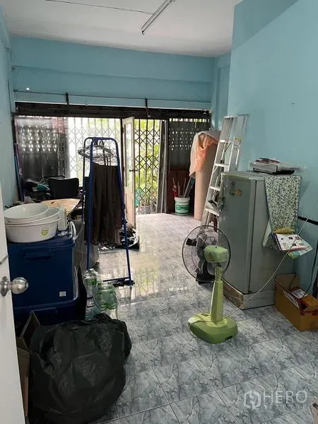 Shophouse for rent in Khlong Toei, Bangkok - Front ground-floor room with light blue walls and sliding metal gate.