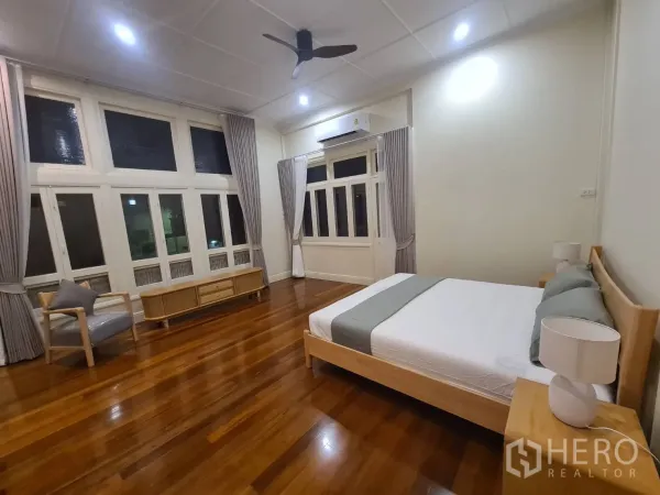 Detached House for rent in Khlong Toei, Bangkok - Spacious master bedroom with large windows, ceiling fan and polished wooden floors.