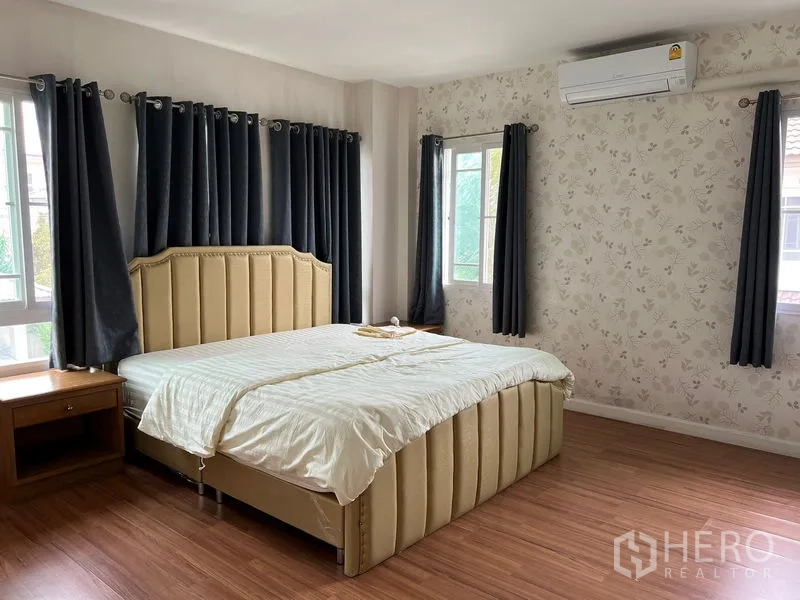 Detached House for rent in Bang Kapi, Bangkok - Spacious master bedroom with king bed, wood floors, wallpaper, multiple windows, and air-conditioning.