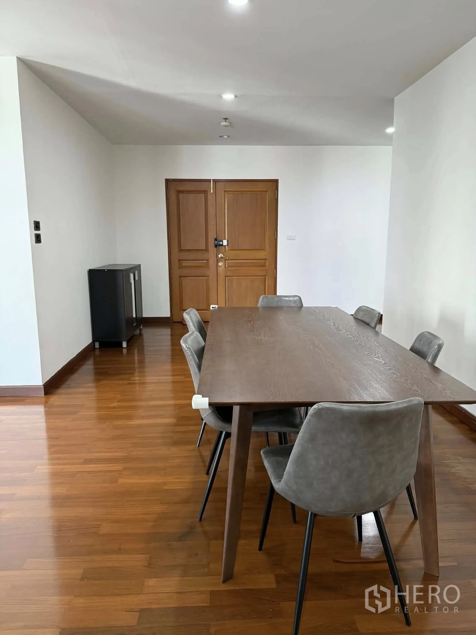 Condominium for rent in Pathum Wan, Bangkok - Dining area with a wooden table and six gray chairs on hardwood floors.