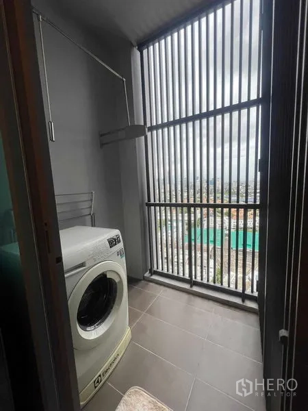 Condominium for rent in Khlong Toei, Bangkok - Utility balcony with washing machine and vertical louver screen overlooking the city.