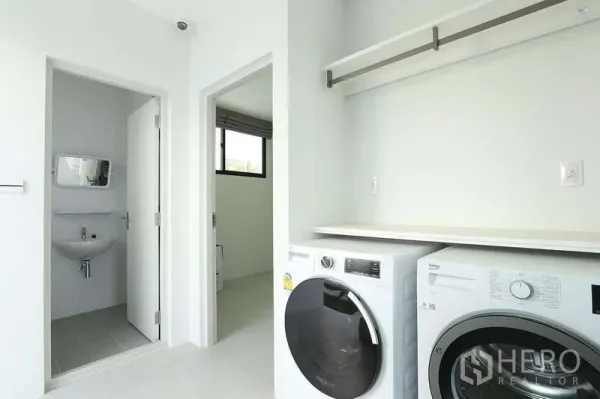 Detached House for rent in Saphan Sung, Bangkok - Bright laundry room with front-loading washer and dryer, open shelf, and door to a compact bathroom.