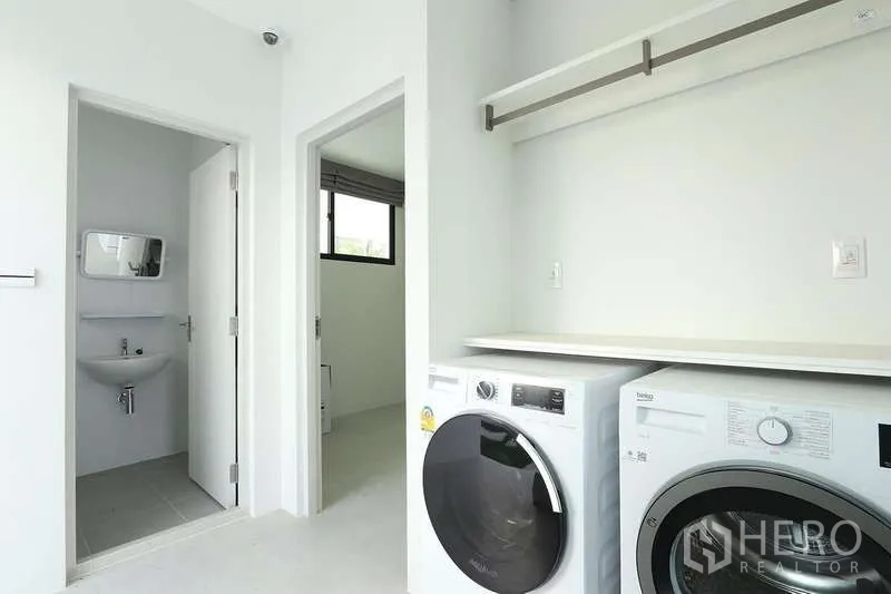 Detached House for rent in Saphan Sung, Bangkok - Bright laundry room with front-loading washer and dryer, open shelf, and door to a compact bathroom.