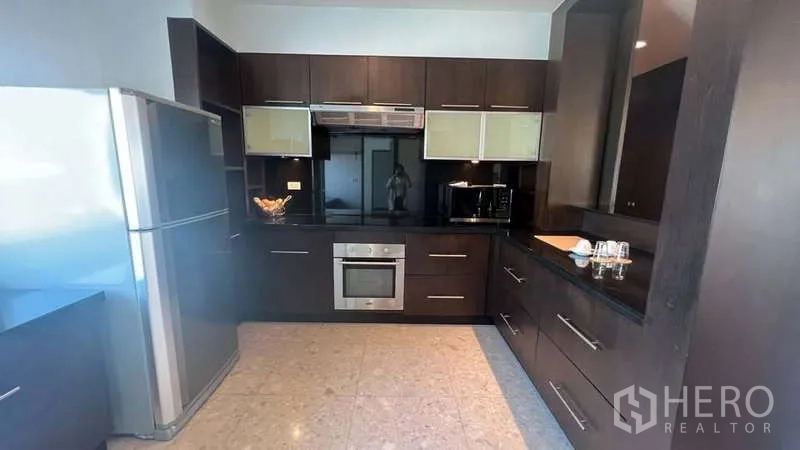 房间 出租在Pathum Wan, Bangkok - 现代封闭式厨房，深色橱柜，不锈钢冰箱、烤箱与黑色台面。