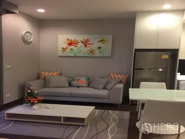 公寓 出租在Ratchathewi, Bangkok - 温馨客厅，灰色沙发、茶几与餐桌，嵌灯照明柔和。