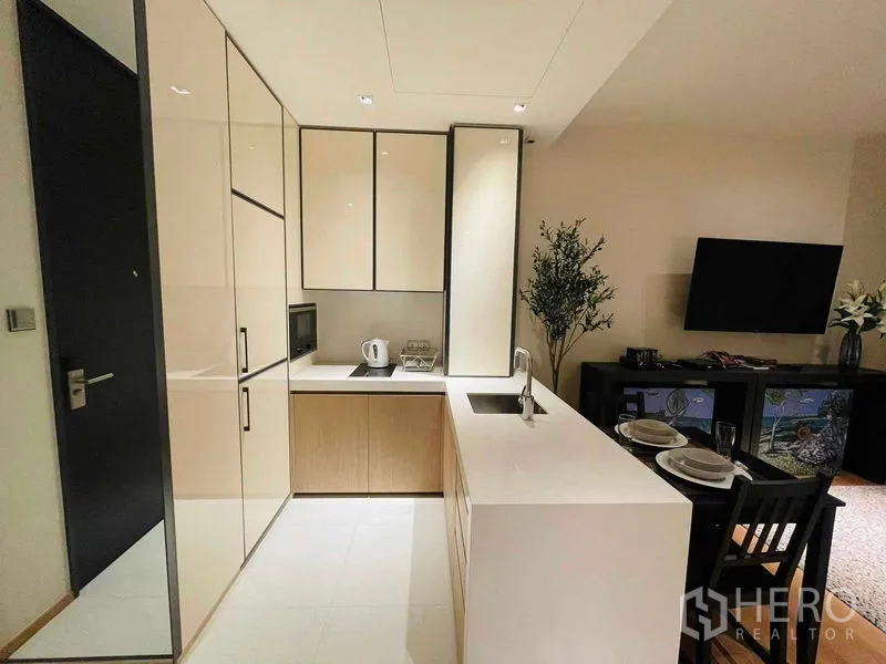 Condominium for rent in Khlong Toei, Bangkok - Compact L-shaped kitchen with white countertops, integrated appliances and sink island.