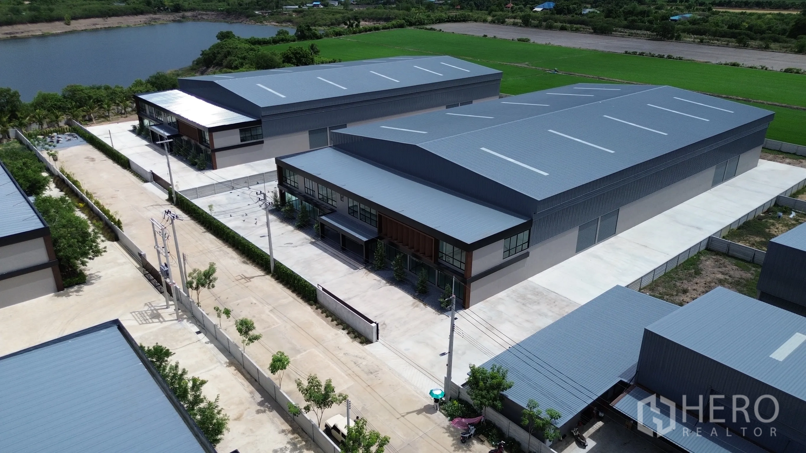 工厂 for rent or sale in Bang Len, Nakhon Pathom - 多栋仓库建筑的航拍图，灰色金属屋顶、园区内部道路、围墙以及周边绿地与水域。