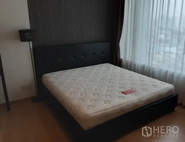 Condominium for rent in Khlong Toei, Bangkok - Bedroom with upholstered bed, wide city-facing window and wood flooring.