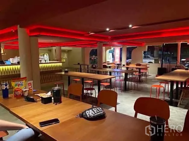 零售空间 出租在Sathon, Bangkok - 一层用餐大厅，长木桌与红色天花灯带的开放式布局。