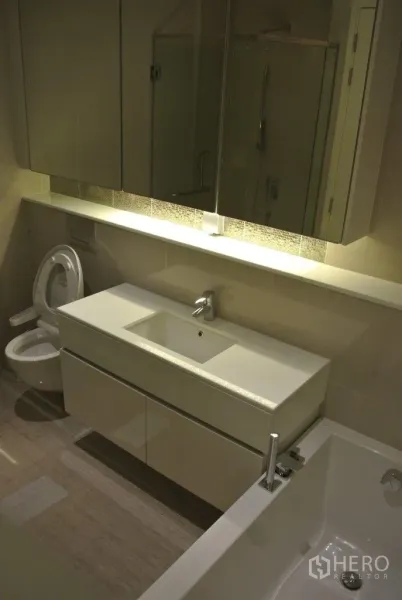 Condominium for rent in Watthana, Bangkok - Modern bathroom with wide vanity, bathtub, toilet and mirrored cabinetry.