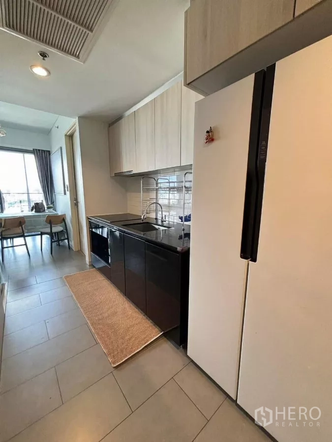 Condominium for rent or sale in Phaya Thai, Bangkok - Galley kitchen with black stone countertop, sink, upper cabinets, and large refrigerator.