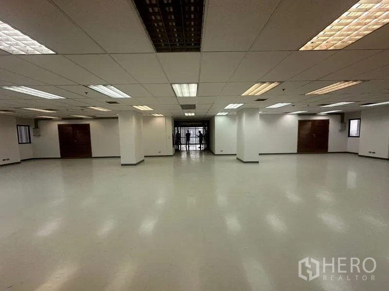 办公空间 出租在Phaya Thai, Bangkok - 宽敞空置办公室，吊顶荧光灯、白色立柱、光滑地面与尽头的玻璃入口。