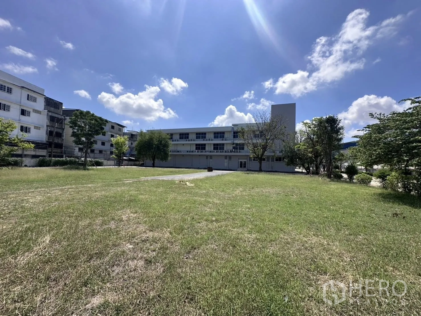 Warehouse for rent in Mueang Samut Prakan, Samut Prakan - Open grassy field in front of the administrative building with surrounding trees.