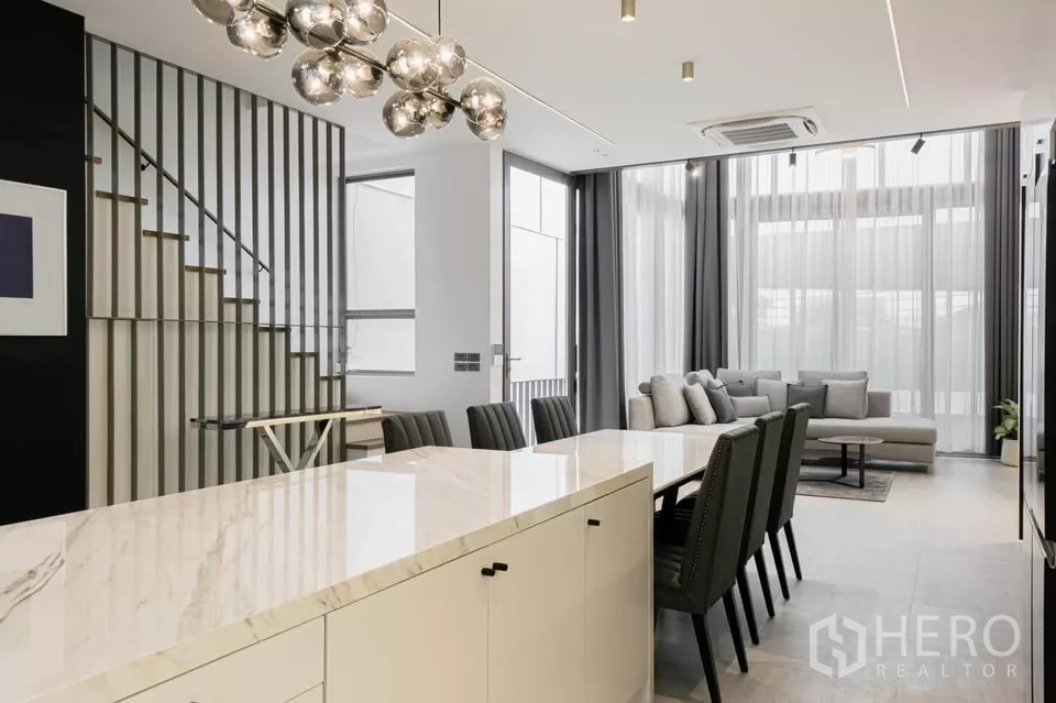 Townhouse for sale in Chatuchak, Bangkok - View from kitchen island to dining set, staircase screen and high-ceiling lounge.