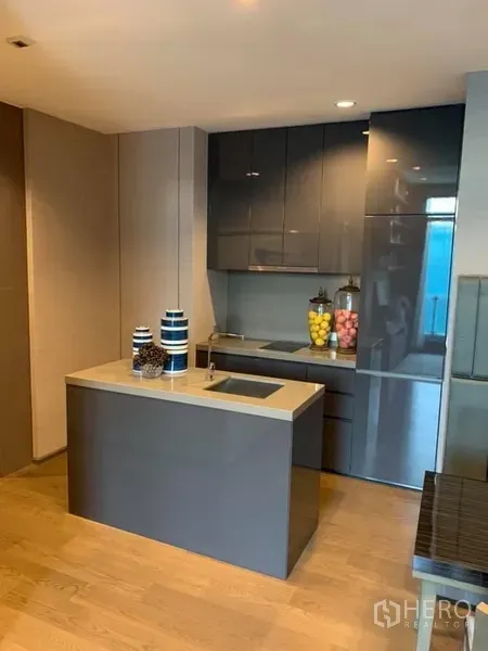 Condominium for rent in Bang Rak, Bangkok - Compact modern kitchen with island sink, glossy cabinets, wood flooring, and integrated appliances.