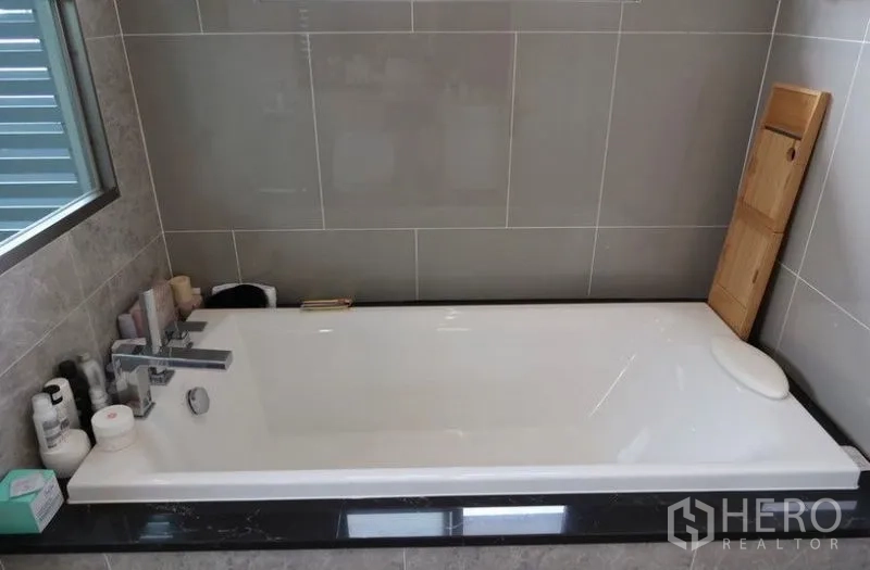 Detached House for rent or sale in Saphan Sung, Bangkok - Contemporary bathtub set against gray tiled walls beside a window.