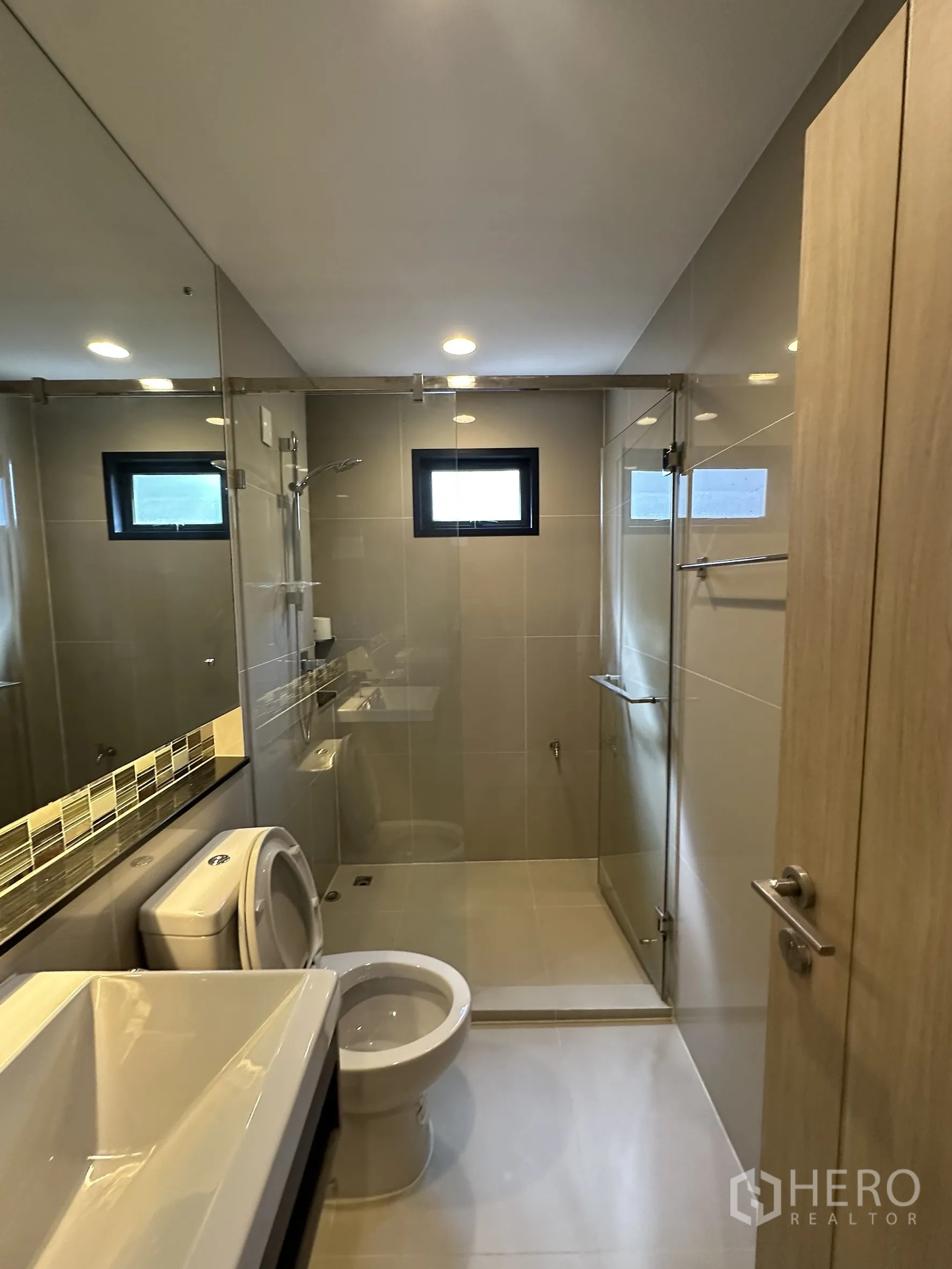 Detached House for sale in Lam Luk Ka, Pathum Thani - Bathroom with glass-enclosed shower, vanity and toilet under recessed lights.